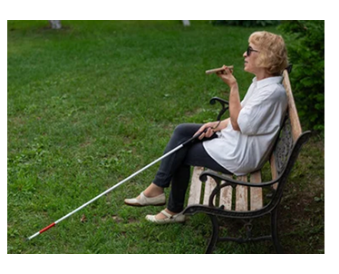 senior woman with white cane on park bench talking on smartphone