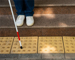 person with cane descending stairs stopping at truncated domes