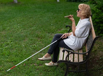 senior woman with white cane on park bench talking on smartphone